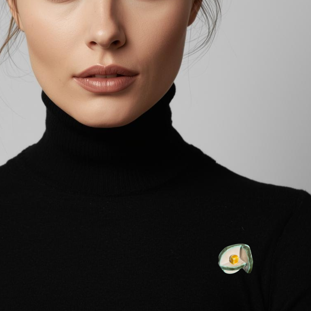 Woman wearing a black turtleneck with a decorative brooch on a plain background