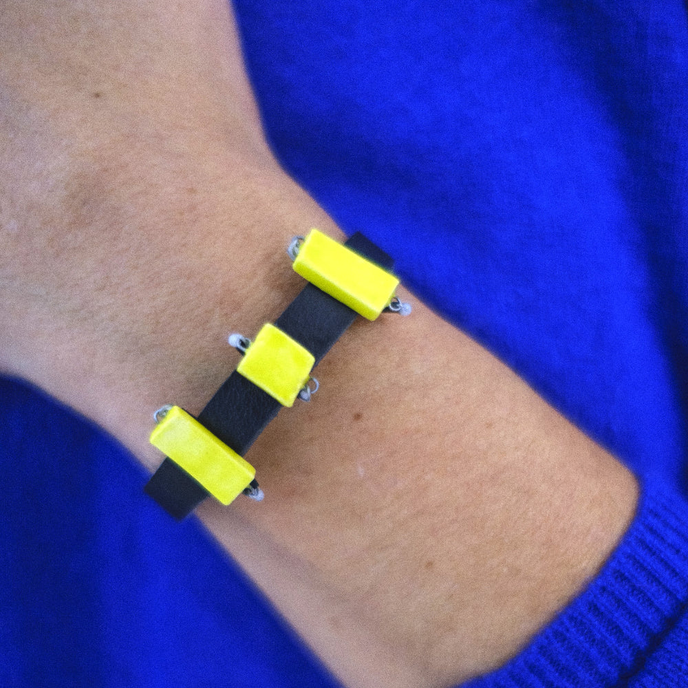 Bracelet with yellow square patterns on a wrist against a blue background