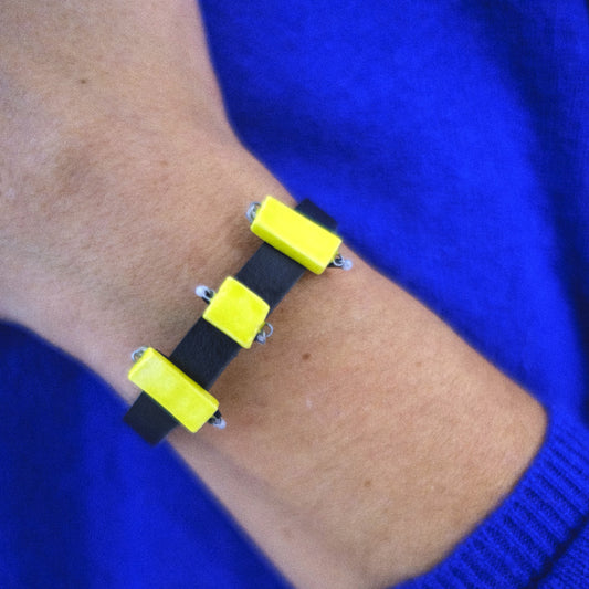 Bracelet with yellow square patterns on a wrist against a blue background