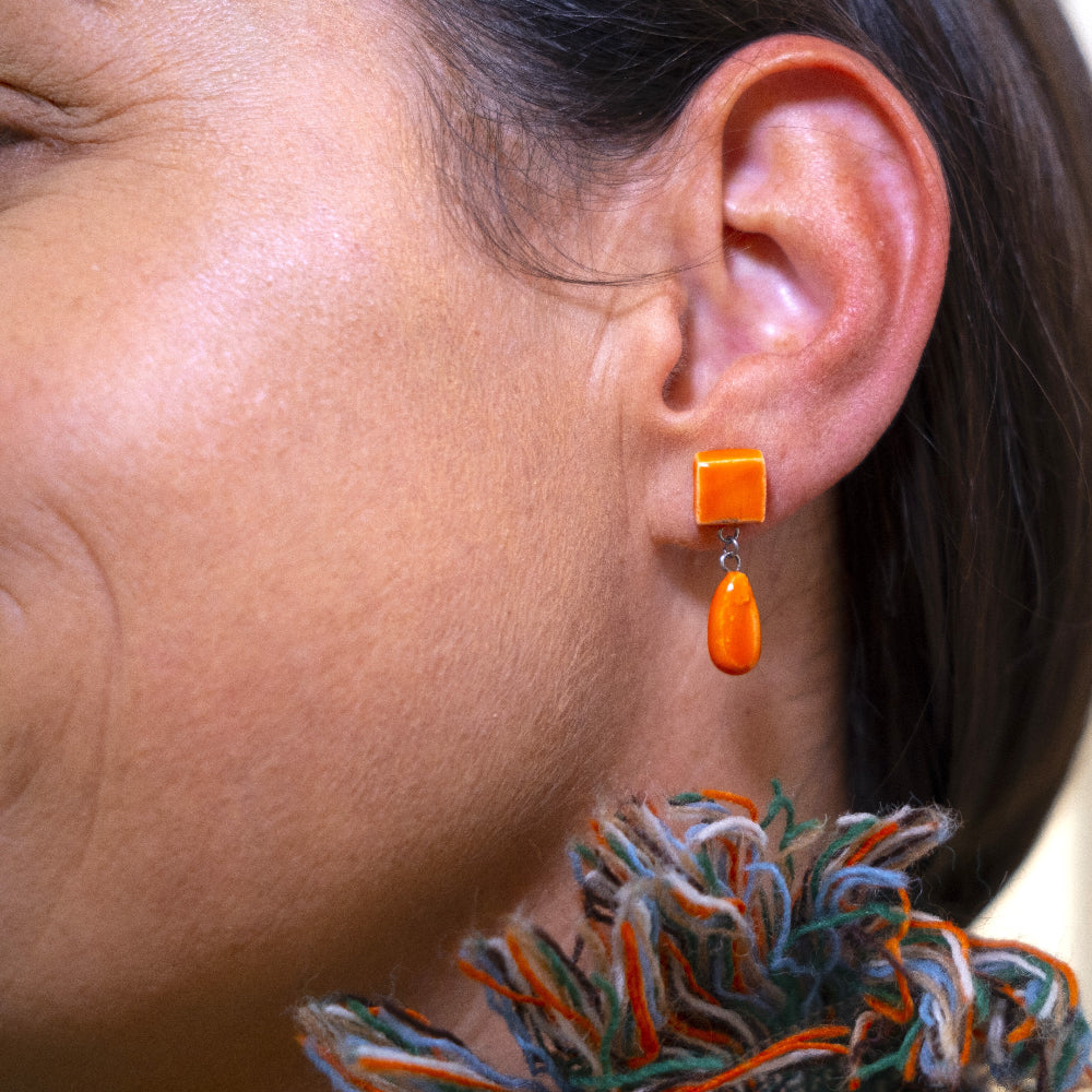Close-up of an ear wearing orange earrings with a blurred background