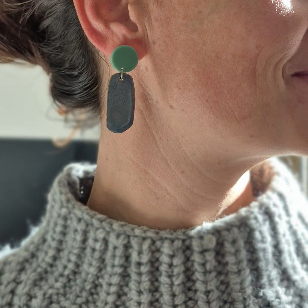 Close-up of a person wearing green earrings with a blurred background