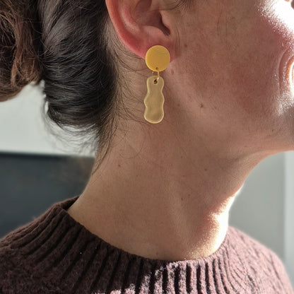 Close-up of a person wearing yellow earrings with a neutral background