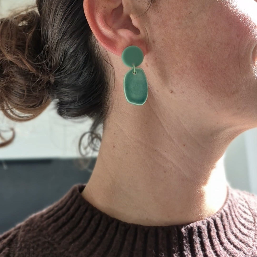 Close-up of a person wearing green earrings with a neutral background