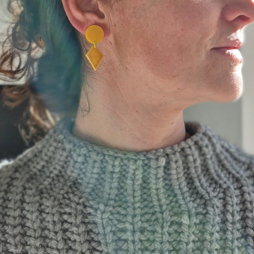 Person wearing yellow earrings with a neutral background