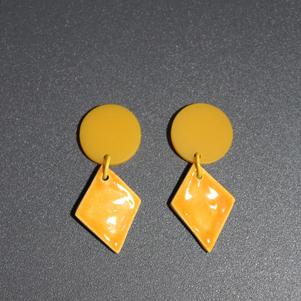 Yellow circular and diamond-shaped earrings on a dark gray background