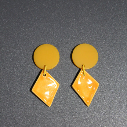 Yellow circular and diamond-shaped earrings on a dark gray background