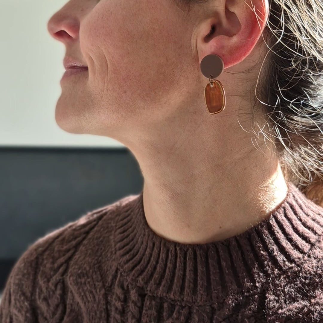 Woman wearing a brown cable knit sweater with earrings, looking to the side.