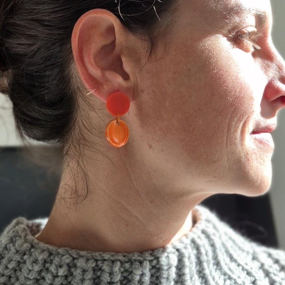 Close-up of a person wearing orange earrings with a blurred background