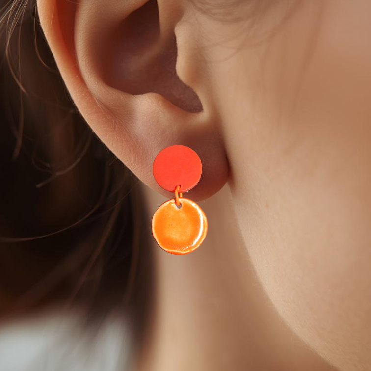 Close-up of an ear wearing a pair of orange earrings with a blurred background