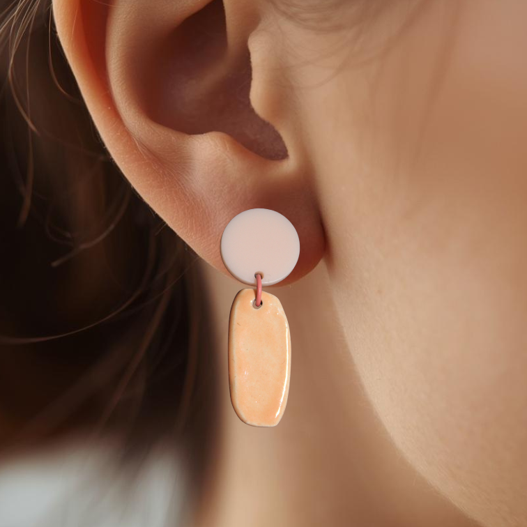 Close-up of an ear wearing a pink and softcoral ceramic earring with a blurred background