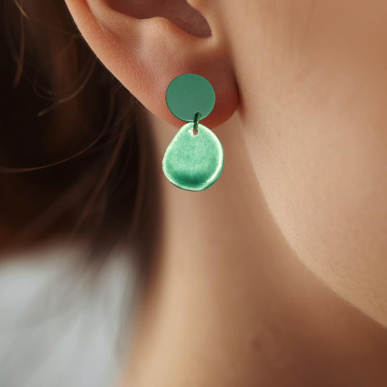 Close-up of an ear wearing a green teardrop earring with a blurred background
