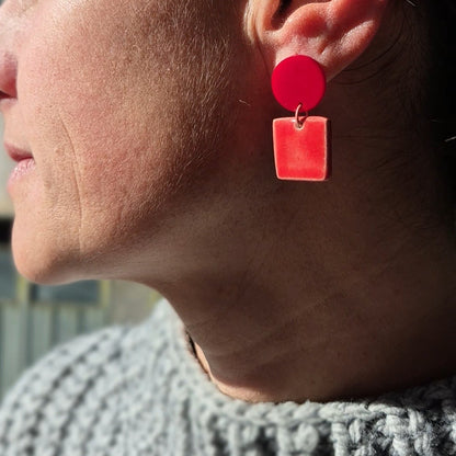 Close-up of a person wearing red earrings with a gray sweater.