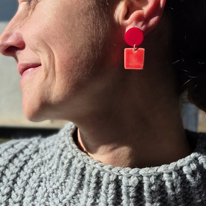 Person wearing red earrings with a gray sweater against a blue sky.
