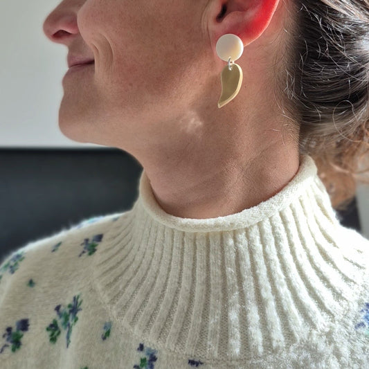 Woman wearing a white sweater with floral patterns, close-up of her ear with earrings.