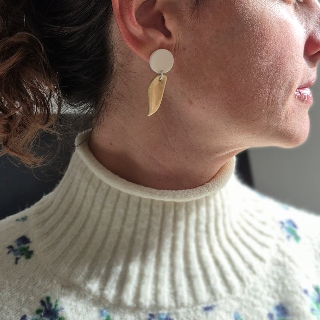 Close-up of a person wearing white and beige ceramic earrings with a floral-patterned sweater.