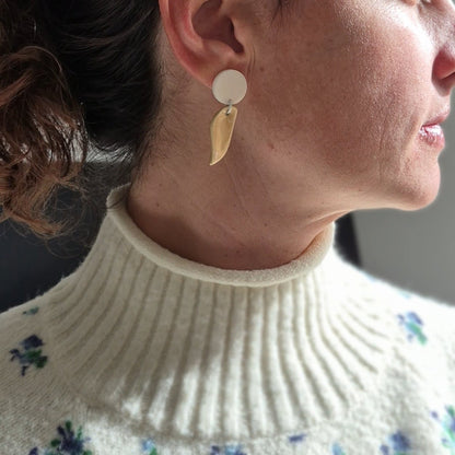 Close-up of a person wearing white and beige ceramic earrings with a floral-patterned sweater.