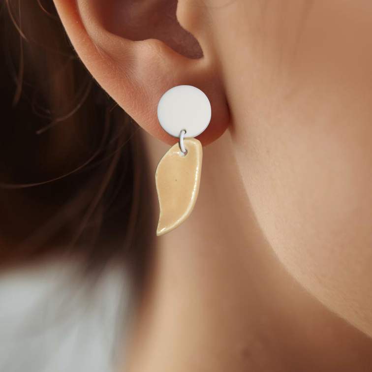Close-up of an ear wearing a white earring with a ceramic leaf detail.
