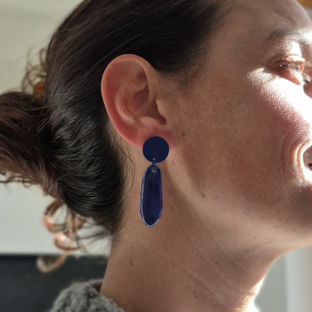 Person wearing blue earrings with a neutral background