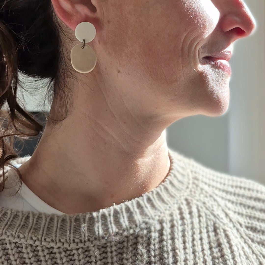 Woman wearing white and  beige earrings, looking to the side.