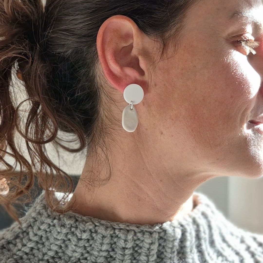 Woman wearing a gray knitted sweater and white earrings, looking to the side.