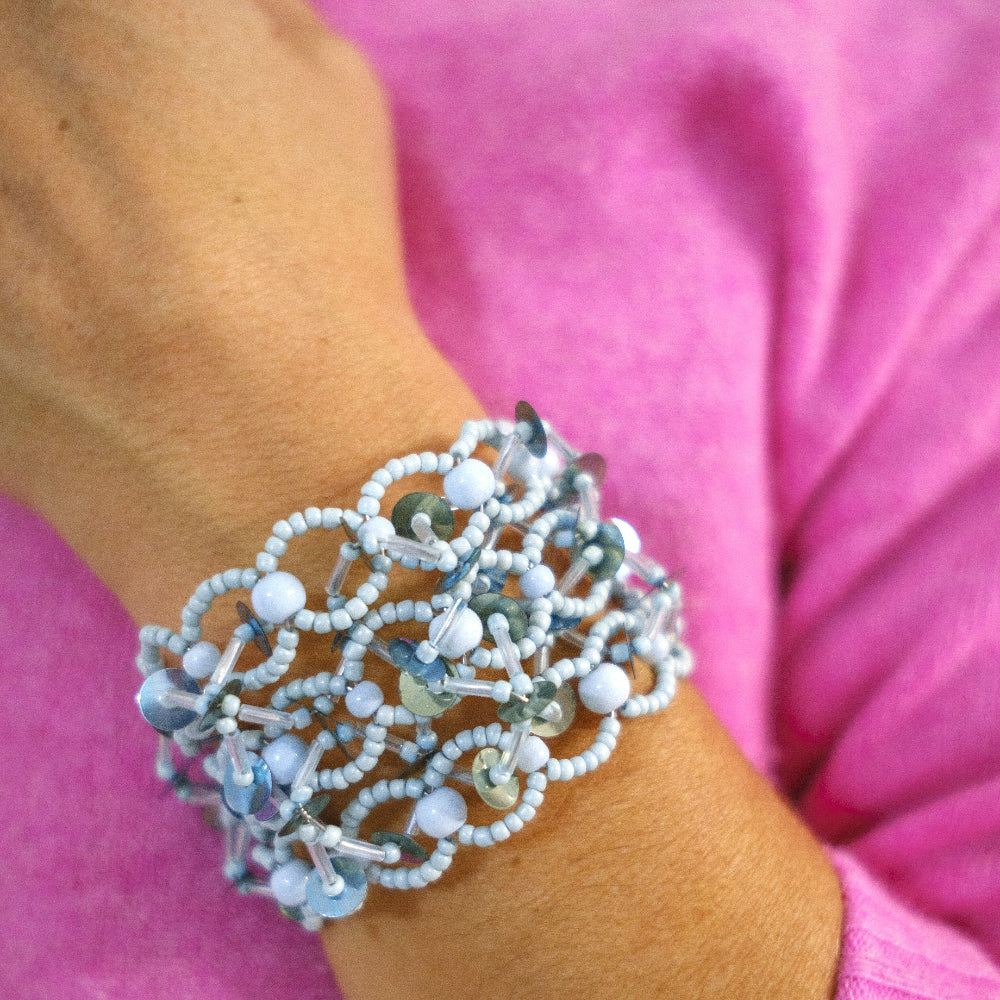 Close-up of a wrist wearing a beaded bracelet with a pink background