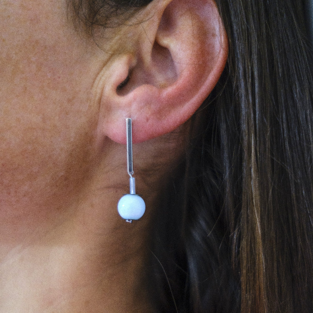 Close-up of an ear wearing a silver earring with a round light blue glass bead.