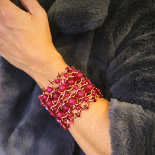 Close-up of a wrist wearing a pink beaded bracelet on a dark fabric background