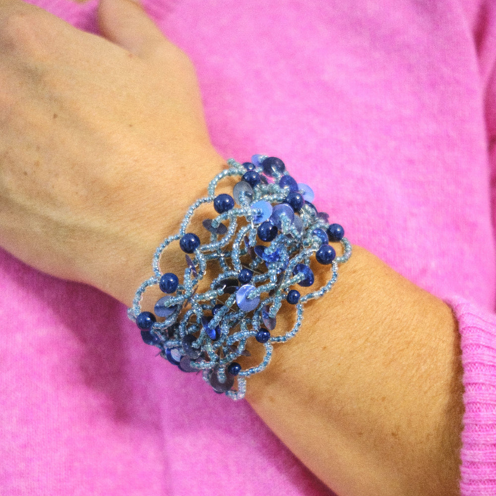 Blue beaded bracelet on a wrist against a pink background