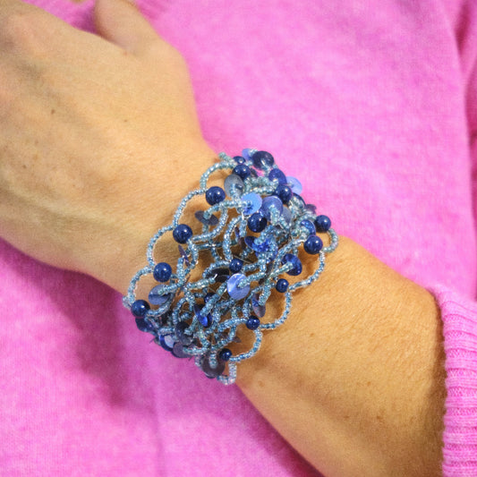 Blue beaded bracelet on a wrist against a pink background