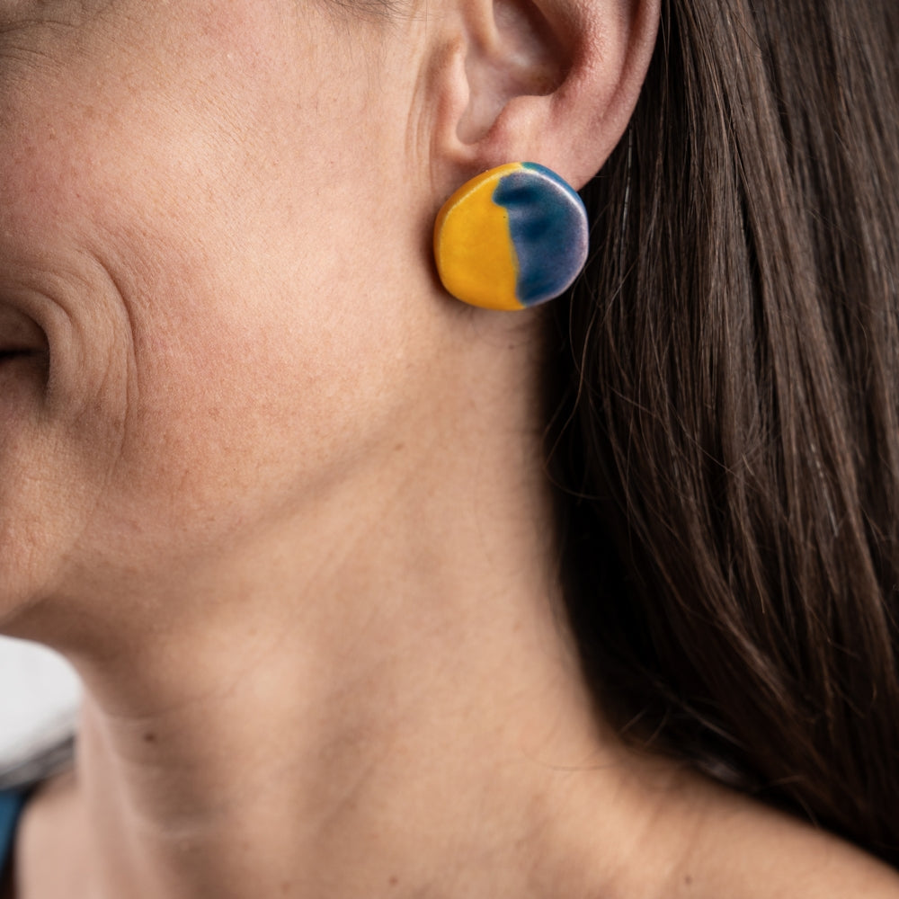 Close-up of a person wearing blue and yellow earrings.