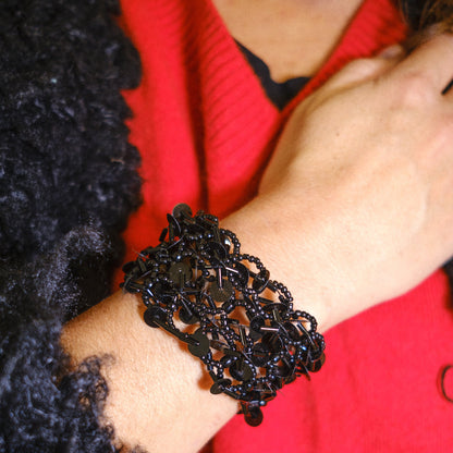 Black beaded bracelet on a wrist with a red  background