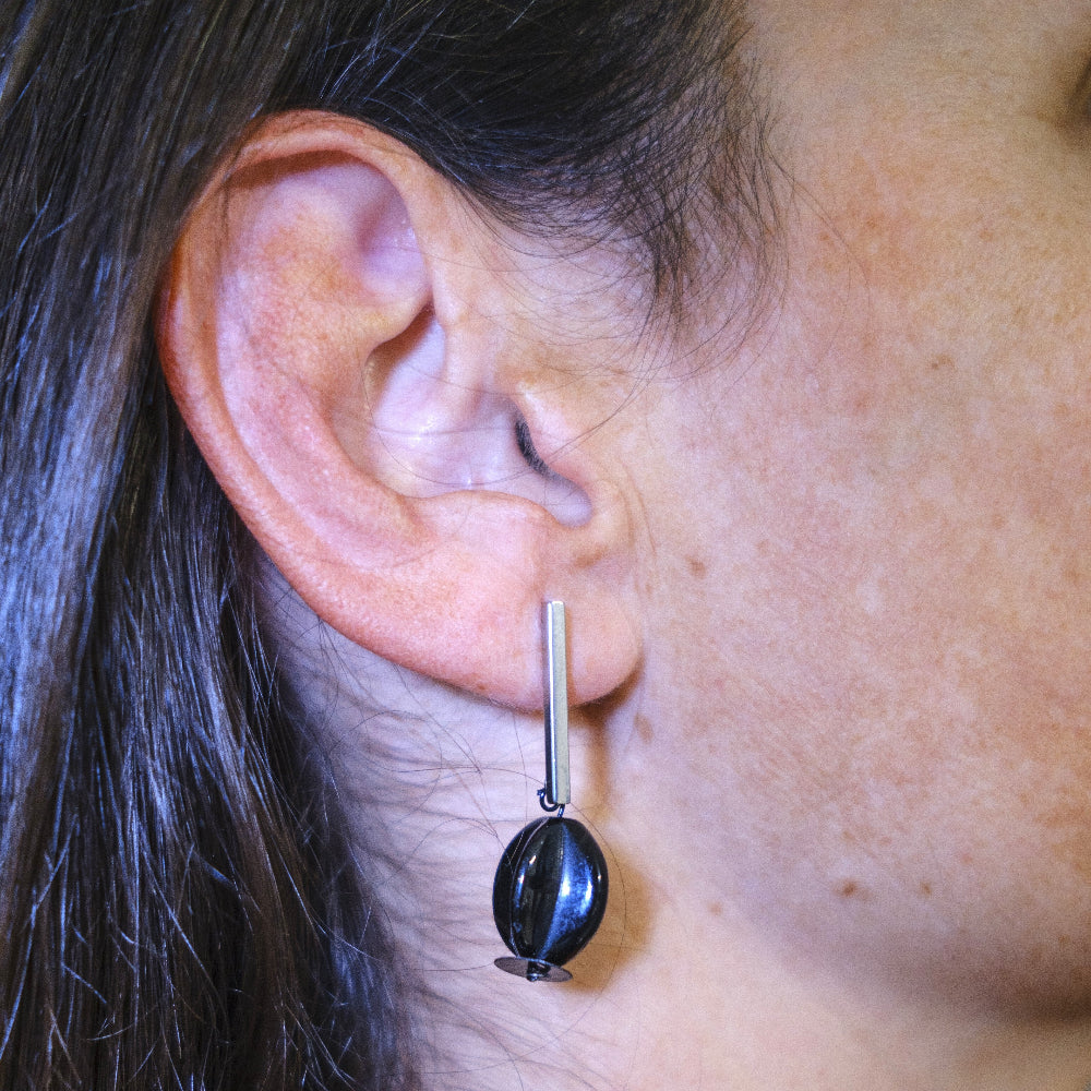 Close-up of an ear wearing a black teardrop earring with a silver bar.