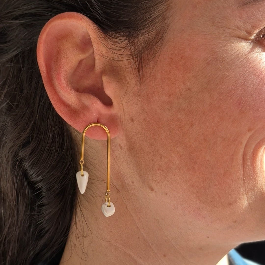 Close-up of an ear wearing a gold earring with geometric ceramic pieces.