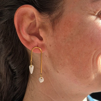 Close-up of an ear wearing a gold earring with geometric ceramic pieces.