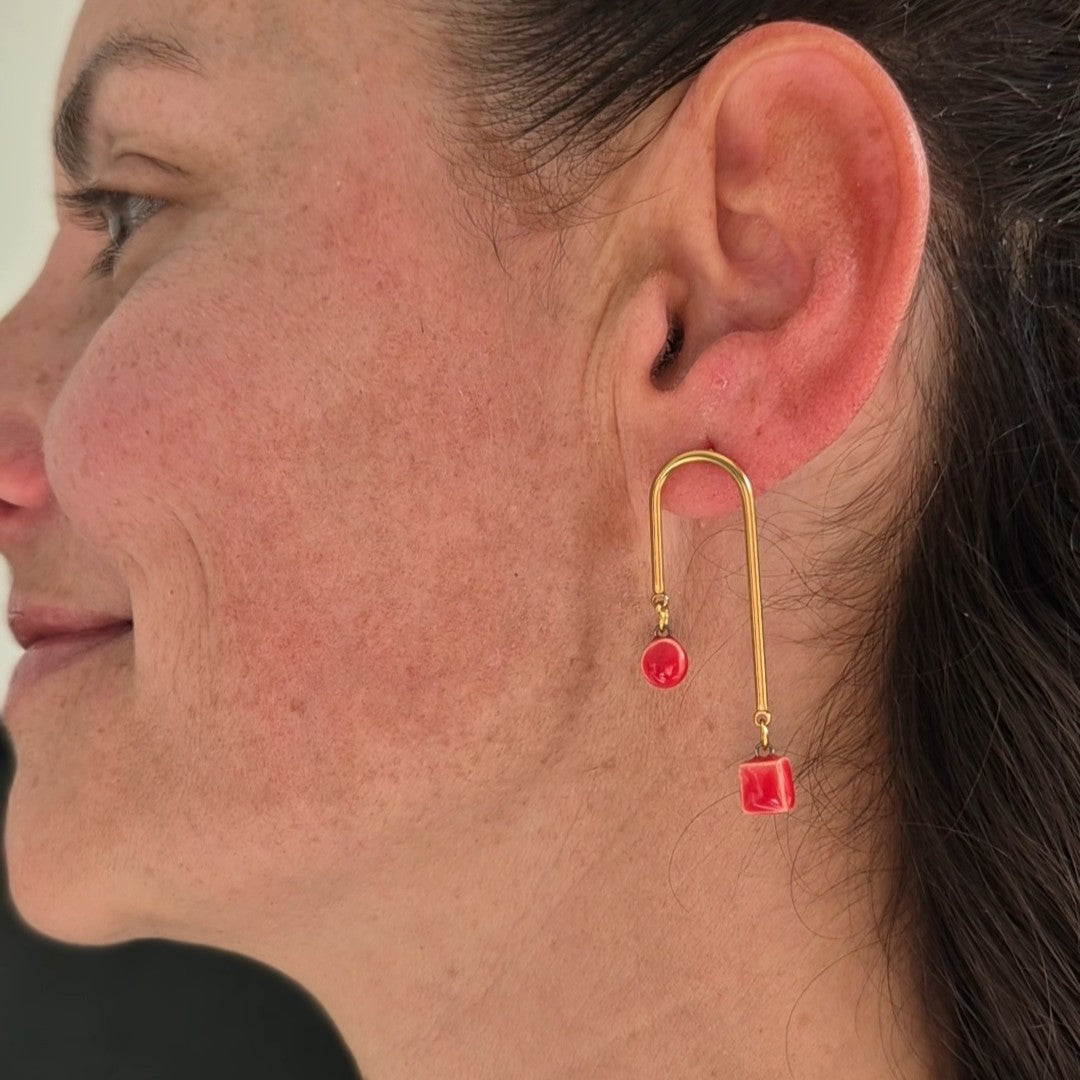 Close-up of a woman wearing gold earrings with red ceramic pieces.