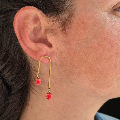 Close-up of an ear wearing a gold earring with geometric red ceramic pieces