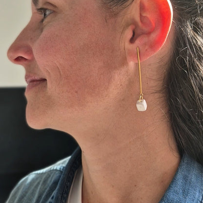 Close-up of a woman wearing a gold earring with a white ceramic cube.