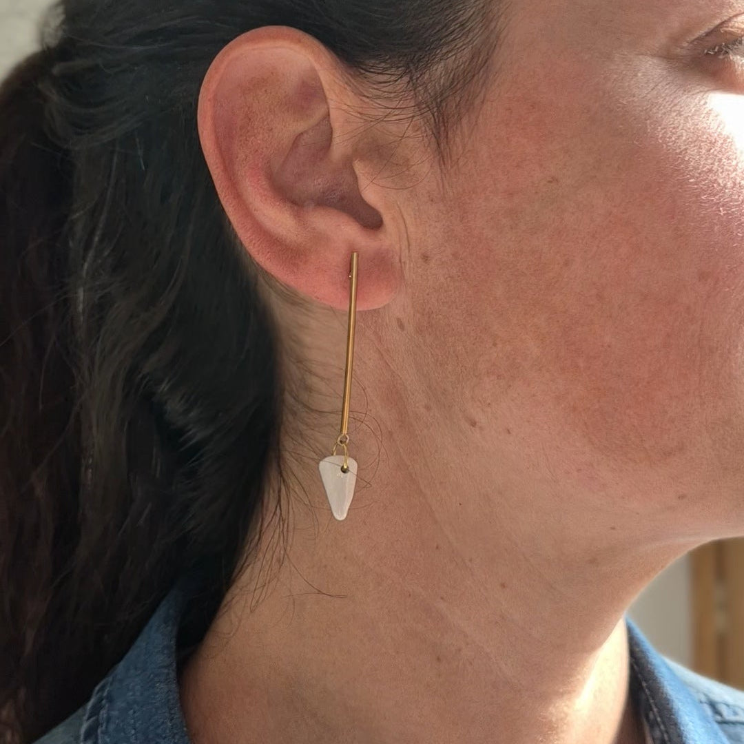 Close-up of a person wearing a gold earring with a white ceramic piece.
