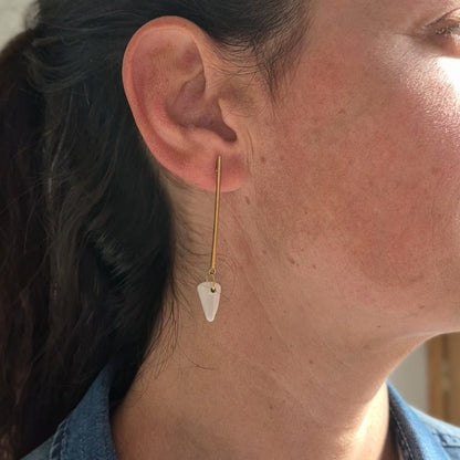 Close-up of a person wearing a gold earring with a white ceramic piece.