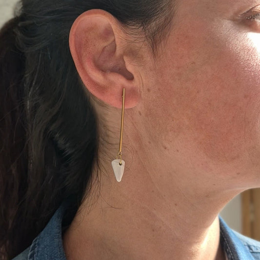 Close-up of a person wearing a gold earring with a white ceramic piece.