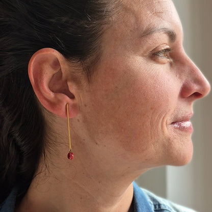 Close-up of a woman wearing a garnet earring, with a neutral background