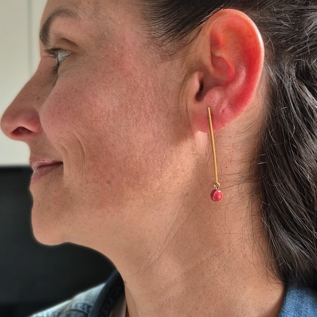 Close-up of a person wearing a gold earring with a rgarnet ceramic piece.