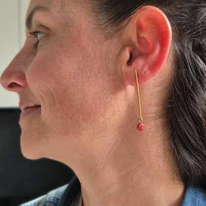 Close-up of a person wearing a gold earring with a rgarnet ceramic piece.