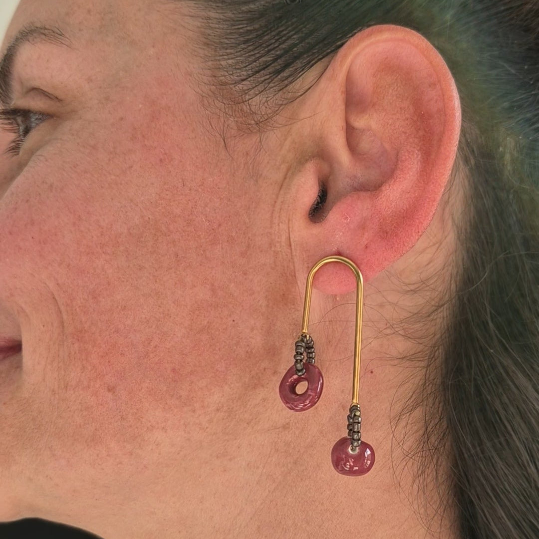 Close-up of a person wearing a gold earring with garnet ceramic  piece.