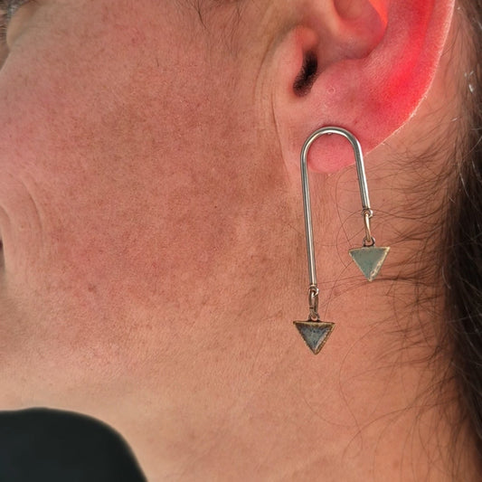 Close-up of a person wearing a silver earring with a triangle design.