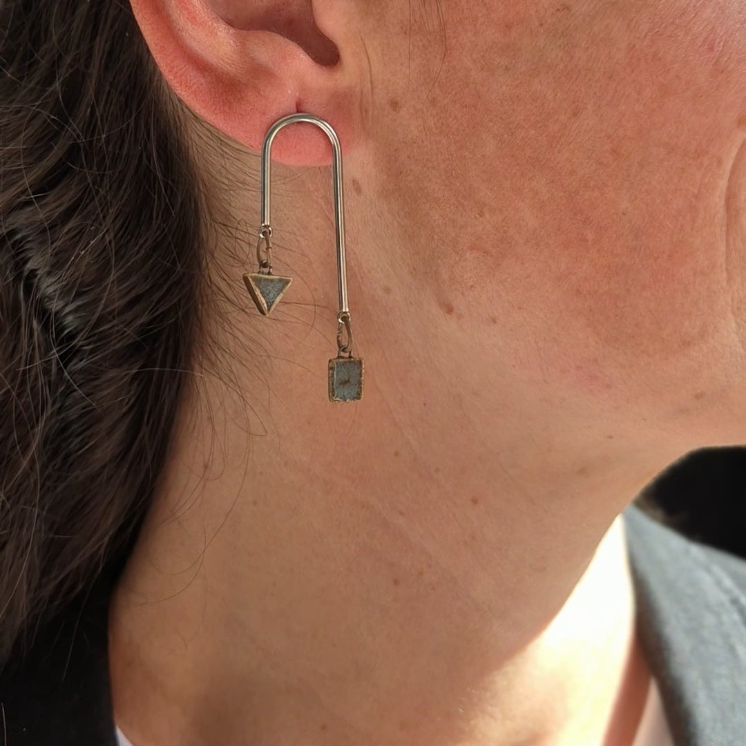 Close-up of an ear wearing a silver earring with grey geometric ceramic pieces.