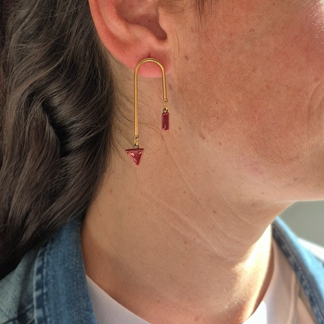 Close-up of a person wearing a gold earring with garnet ceramic pieces.