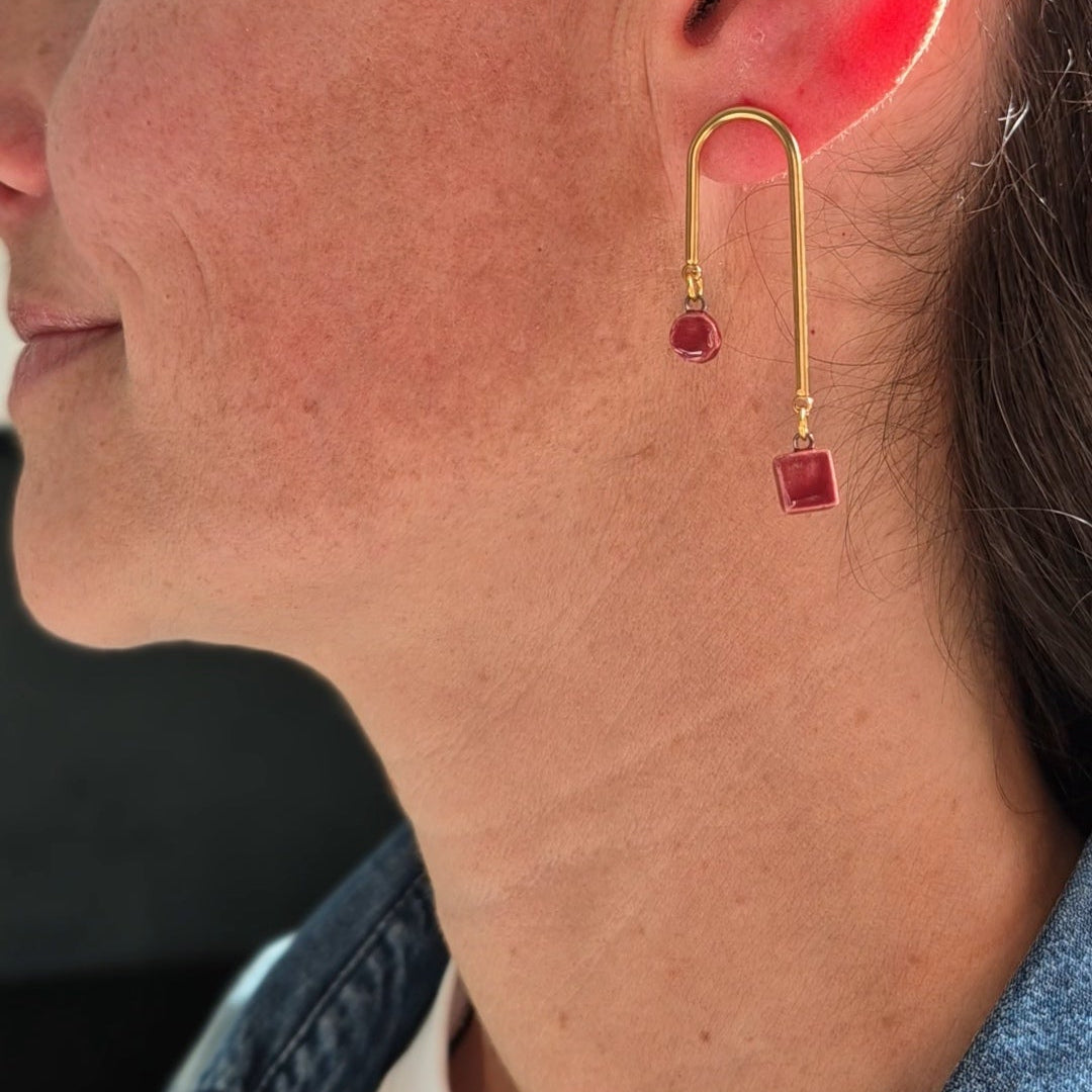 Close-up of a woman wearing gold earrings with garnet ceramic pieces. Focusing on the ear and part of the face.