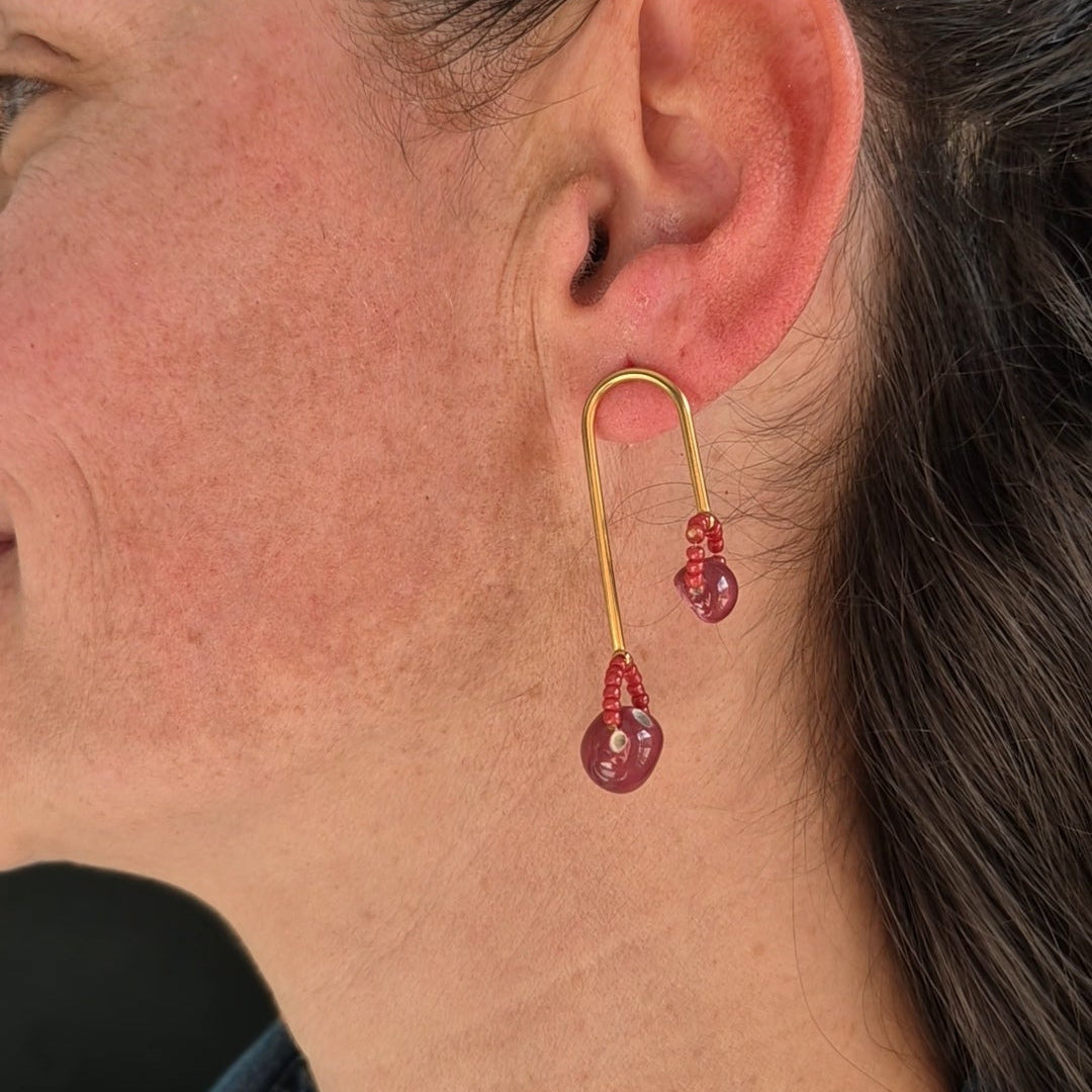 Close-up of an ear wearing a gold earring with ceramic and beads.
