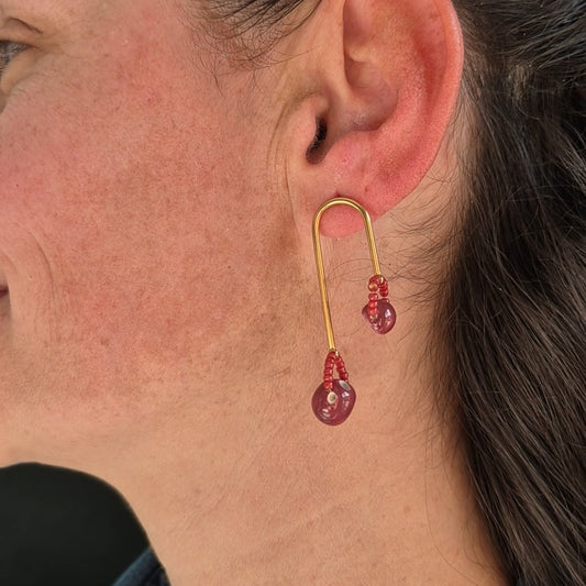 Close-up of an ear wearing a gold earring with ceramic and beads.